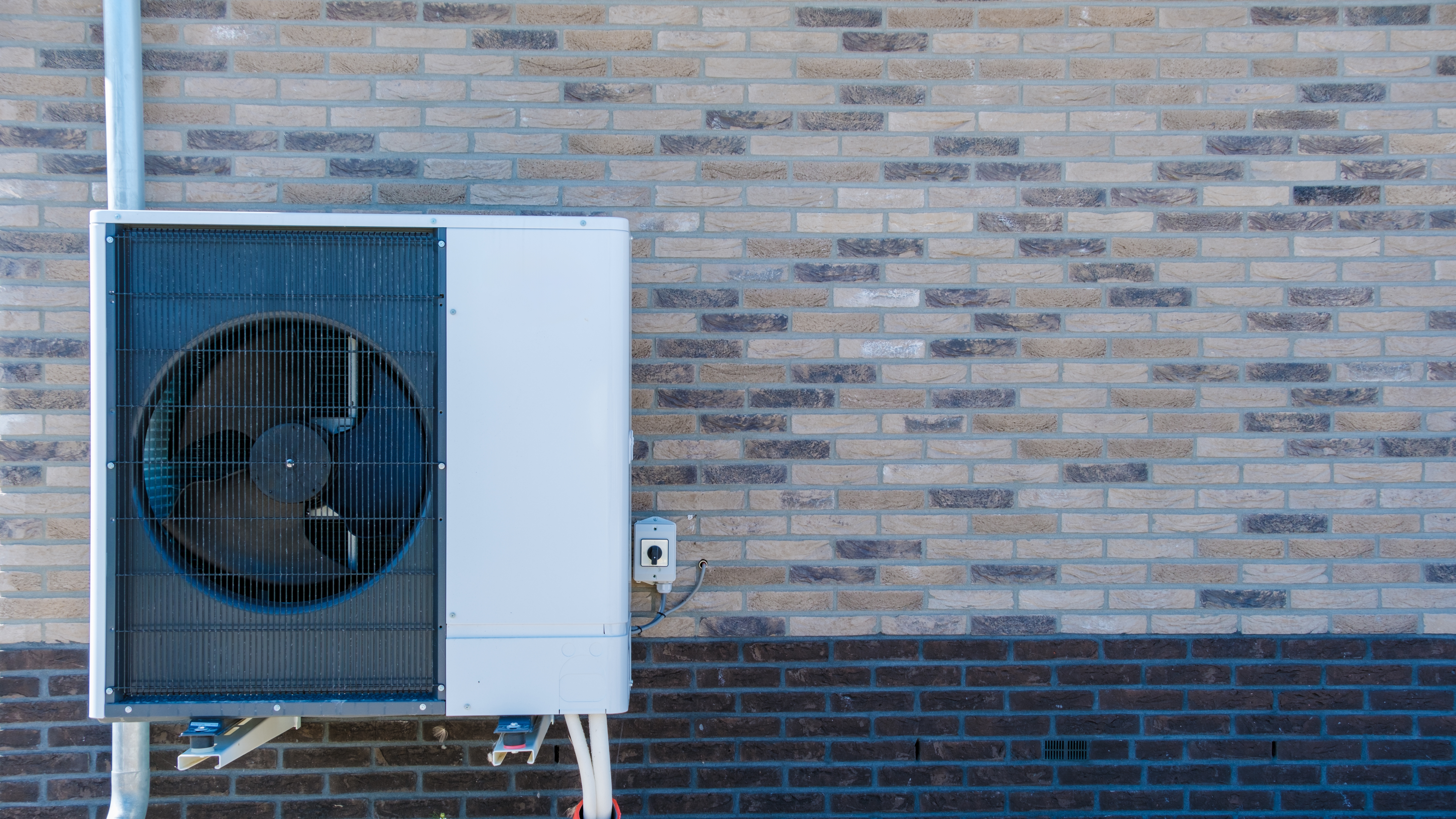 A modern air source heat pump mounted on a brick wall